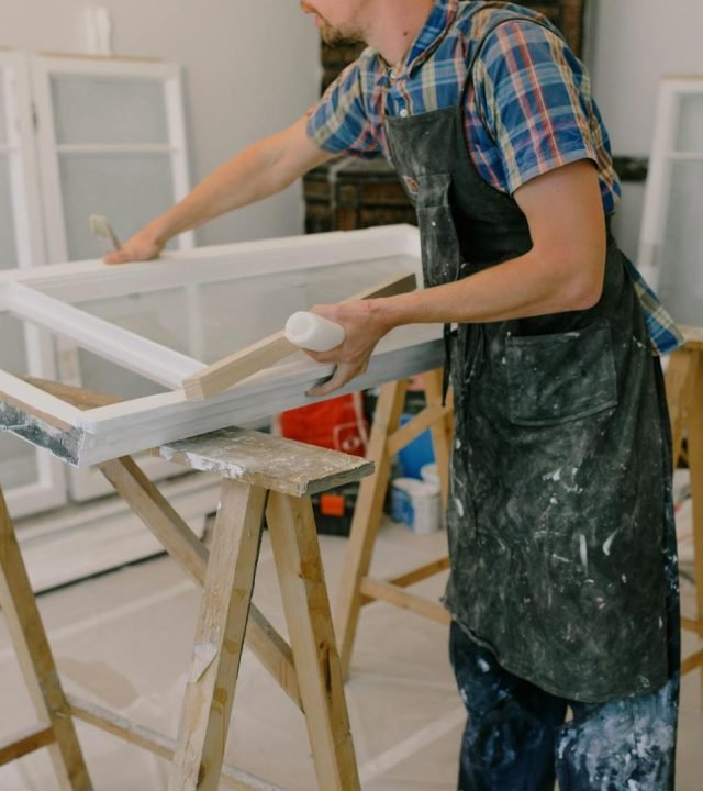 A skilled craftsman repairing a window frame indoors using tools and expertise.